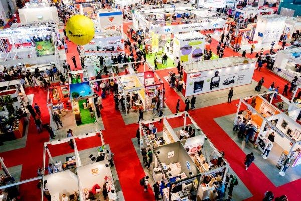 Wide exhibition hall floor with rows of booths and visitors